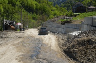 Car drives along a dirt road in a rural mountain landscape, on the way to the Goderdzi Pass near