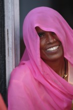 Smiling woman, face partly covered by long, scarf-like pink shawl or Dupatta, also known as Chunni,