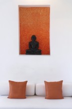 Statue of a black Buddha sitting meditating against an orange background, including bed with