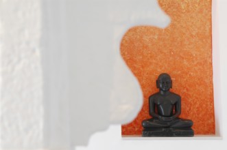 Statue of a black Buddha sitting meditating against an orange background, Devigarh Palace Hotel,