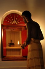 A man prays in front of a small shrine with a burning flame, spiritual atmosphere in warm light,