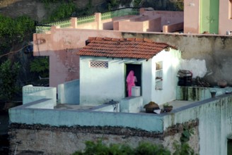 A woman wearing pink sari stands on the roof of a turquoise house, PDorf Delwara near Udaipur,