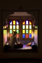 Woman sitting cross-legged reading in a room with colorful windows, calm and contemplative