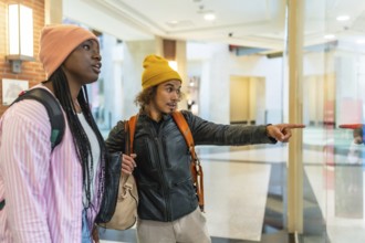 Young friends window shopping in a bright modern mall, pointing at a boutique display through