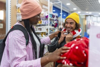 Diverse young couple shopping together in a store, smiling and trying on a neck pillow while