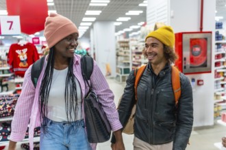 Diverse young couple smiling while holding hands, walking together down an aisle in a retail store