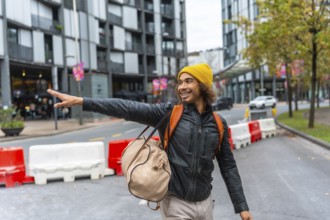 Happy young multiracial man wearing a yellow beanie and leather jacket pointing with his hand while