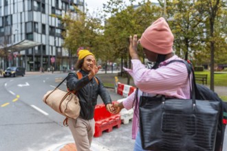 Young diverse couple extending hands for a high five, holding hands, and carrying bags while