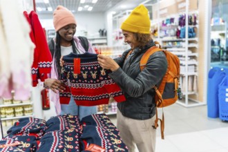Young couple browsing festive reindeer sweater in a bright store, smiling as they choose holiday