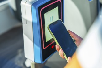 Person using mobile phone for contactless payment on a bus or public transport turnstile,