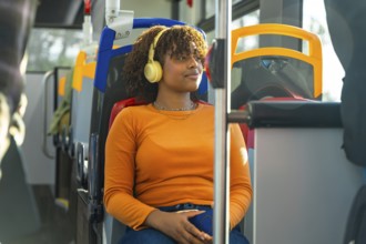 Young black woman with afro headphones relaxes and listens to music on a city bus during her