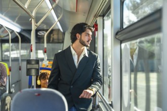 Young businessman in a suit jacket stands by a transit window, looking out pensively as the city
