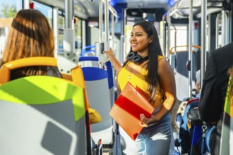 Young woman smiling, standing inside a modern public transportation bus, holding an orange binder
