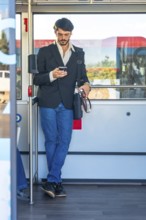 Young man standing on a crowded bus, absorbed in his smartphone as he scrolls and messages during a