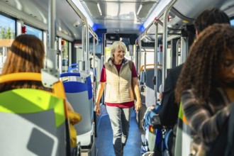 Senior woman smiling and walking along the aisle of a public bus, passengers traveling and sitting