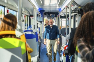 Senior man smiling and looking at the camera while walking down the aisle of a public bus, with