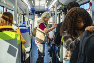 Senior woman standing inside a crowded city bus, holding a handrail among diverse commuters during