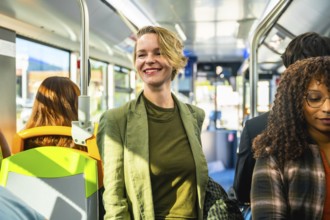 Woman standing on crowded city bus, smiling and holding the railing during a bright, stress free