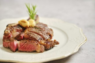 Juicy grilled cowboy steak on a decorative plate, enhanced with fresh herbs and garlic. This dish