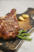 A mouthwatering grilled steak is placed on a weathered wooden cutting board. Fresh rosemary and