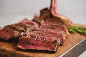 Close-up view of sliced grilled t-bone steak medium rare on a wooden cutting board. The meat is