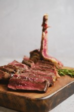Thick slices of perfectly cooked t-bone steak medium rare on a wooden cutting board. Fresh herbs