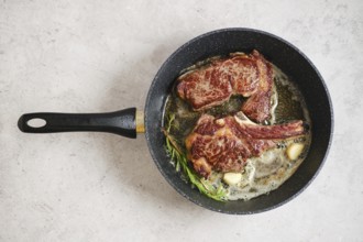 Two steaks - ribeye roll and cowboy sizzle in a skillet, surrounded by melted butter and fresh