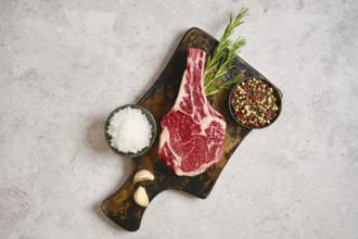 A fresh cowboy steak on a wooden cutting board, surrounded by garlic cloves, coarse salt, and a