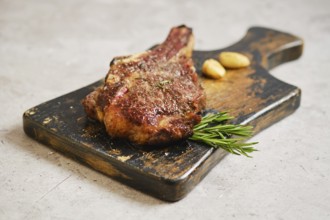 A perfectly cooked cowboy steak on a rustic wooden cutting board, garnished with fresh rosemary and