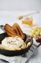 A baked cheese dish is elegantly presented in a cast iron skillet alongside toasted bread and fresh