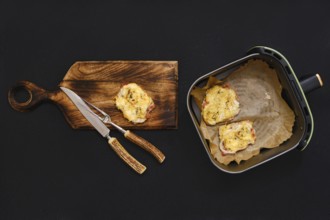 Golden-brown pork chops are placed on a wooden cutting board next to an air fryer