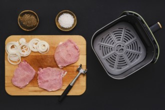Raw pork chops on a wooden cutting board next to mallet. Sliced onions are ready beside them, with