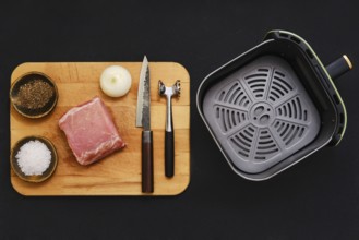 Raw pork tenderloin on a wooden cutting board alongside seasonings and kitchen tools. An onion,