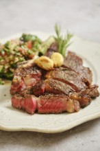 Juicy grilled steak rests on a decorative plate, served alongside a fresh salad made with vibrant