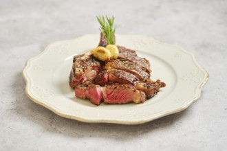 Tender grilled cowboy steak cut into slices on a decorative plate. It is garnished with herbs and
