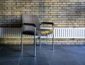 Retired and broken old office chair stands in front of a small radiator in an office building,