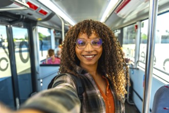 Young woman with curly hair and glasses smiling at camera while taking a happy selfie on a city