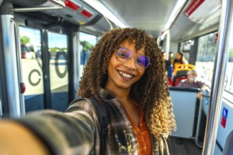 Young happy woman with curly hair wearing glasses and a plaid shirt, taking a selfie while