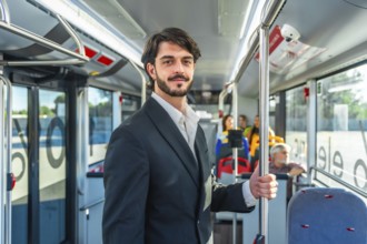 Young businessman traveling by bus, holding a pole and smiling while looking at the camera, with