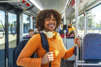 Smiling black woman commuter standing on a city bus, headphones on and backpack ready, embodying