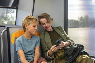 Mother and son sharing a smile as they browse a smartphone together on a city bus, enjoying a