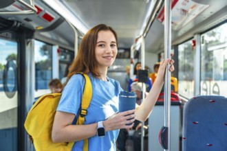 Young woman smiling on a city bus, standing and holding a pole with a yellow backpack and reusable