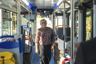 Senior man with a beard and plaid shirt standing in the aisle of a public bus, commuting during the