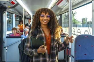 Young black woman student smiling at the camera while standing inside a public transportation bus,