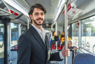 Young businessman smiles confidently while standing and holding a pole on a crowded city bus,