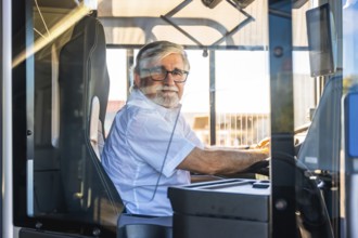 Senior man with a white beard and glasses wearing a shirt, sitting at the driver's seat of a modern