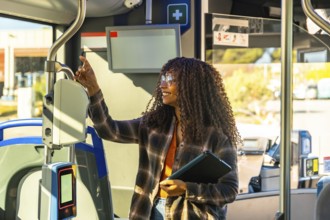 Young black woman holding a digital tablet and validating her public transport ticket on a modern