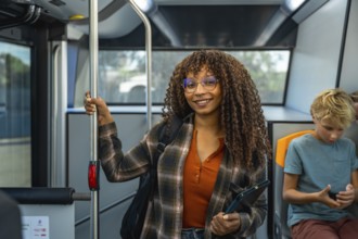 Young black woman with curly hair wearing glasses and a plaid shirt, smiling at camera, holding