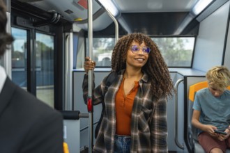 Woman with afro hair and eyeglasses standing and holding a handrail on a public transport bus,