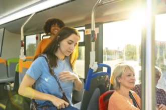 Diverse commuters on a city bus in sunlight, young woman looking down while other passengers sit